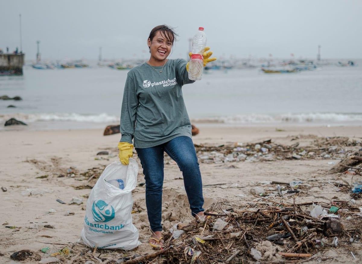 A collector smiling with a bag of plastic on a beach in Indonesia